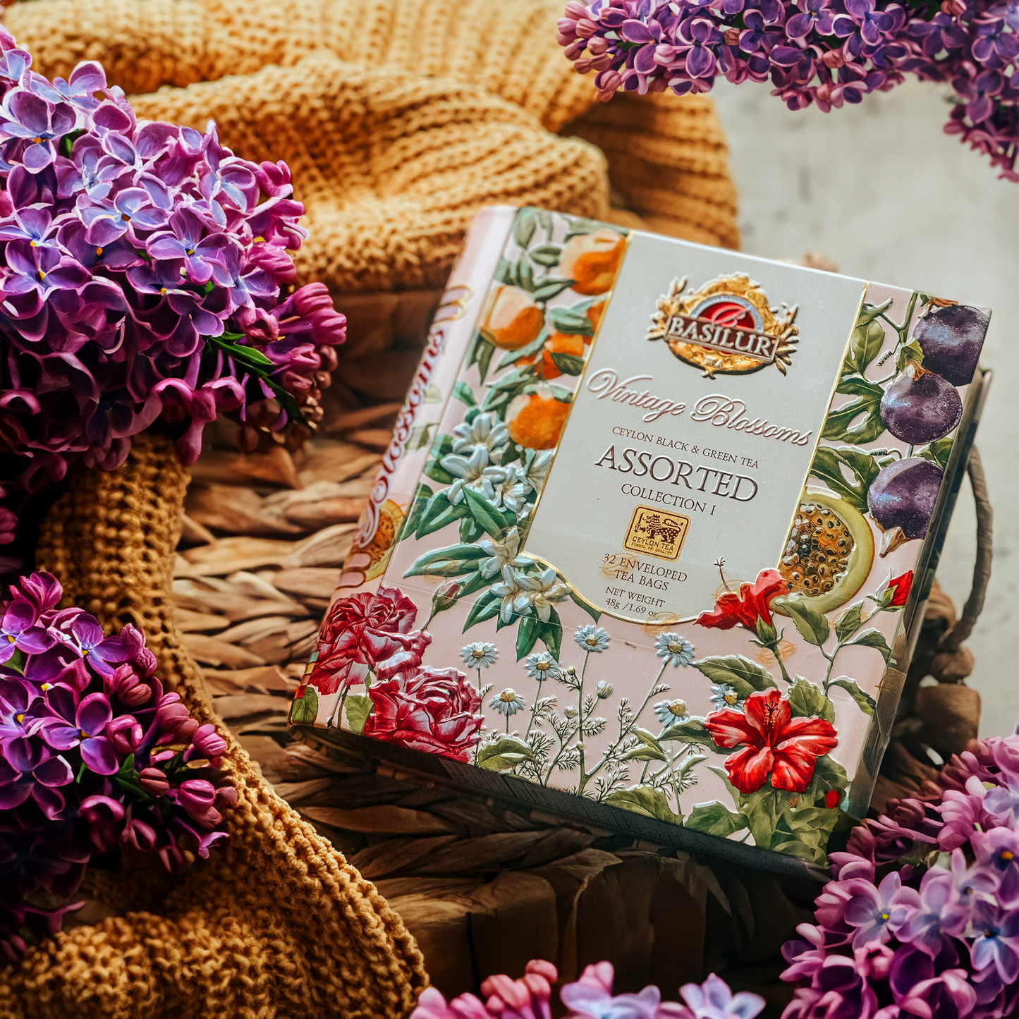Eleganckie pudełko herbat Basilur Vintage Blossoms Assorted wśród kwiatów i dzianiny, ozdobne opakowanie na tle wikliny