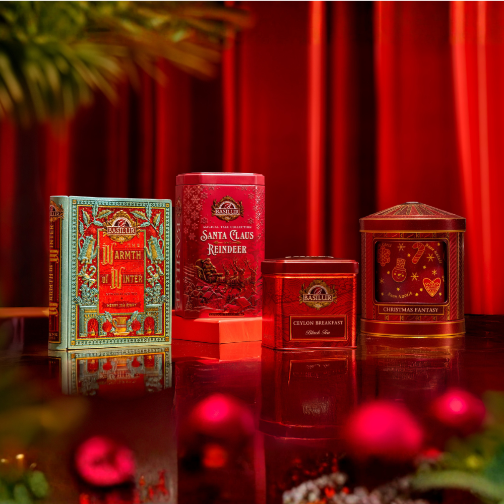 Zestaw świątecznych herbat Basilur w ozdobnych puszkach na tle czerwonych dekoracji.