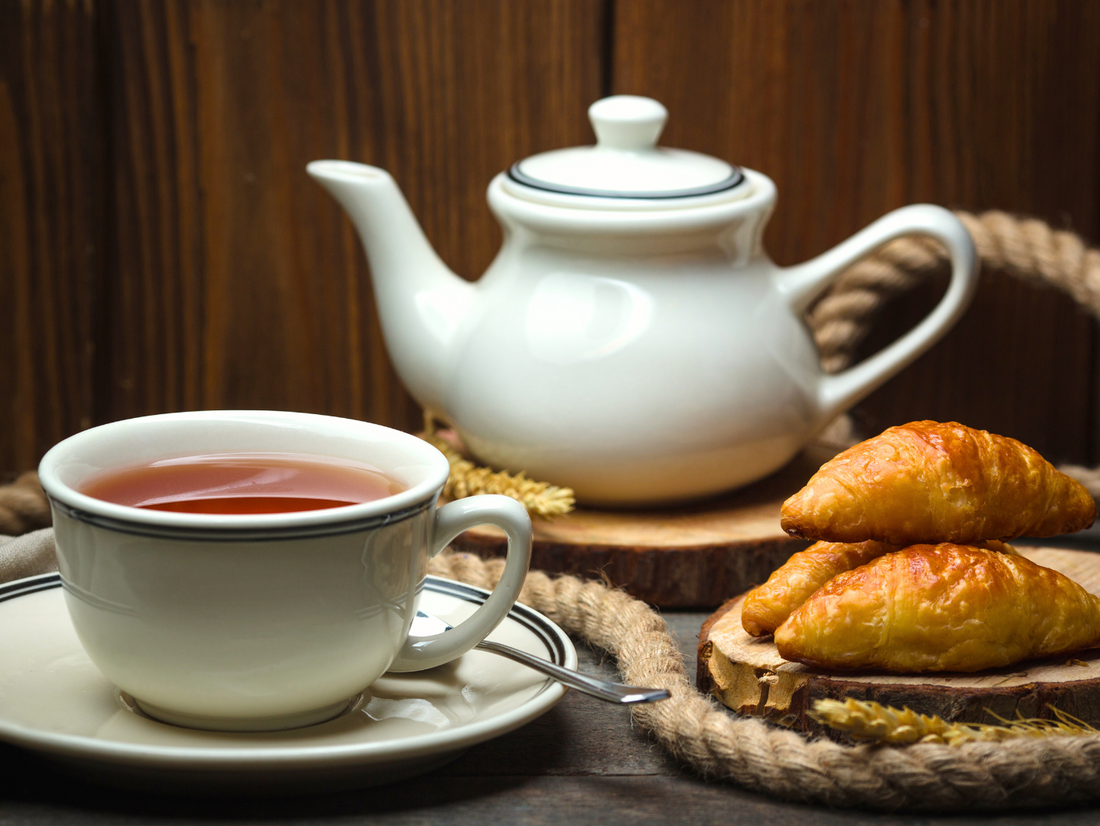 Filiżanka czarnej herbaty podana z croissantami.