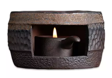 Podgrzewacz ceramiczny okrągły 9 cm w kolorze ciemnym, z palącą się świeczką tealight wewnątrz.
