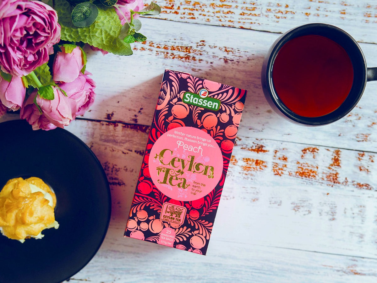 Pudełko herbaty Stassen Peach Tea obok filiżanki naparu na drewnianym stole.