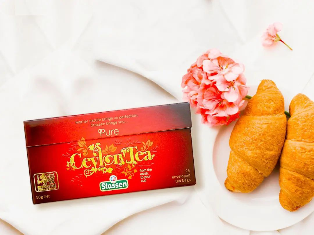 Pudełko herbaty Stassen Pure Ceylon z croissantami i kwiatami, elegancka kompozycja.