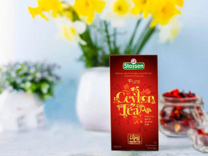Herbata Stassen Pure Ceylon z kwiatami w tle, eleganckie pudełko herbaty cejlońskiej.