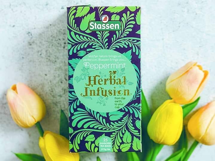Pudełko herbaty Stassen Peppermint Herbal Infusion 25 kopert obok żółtych tulipanów.