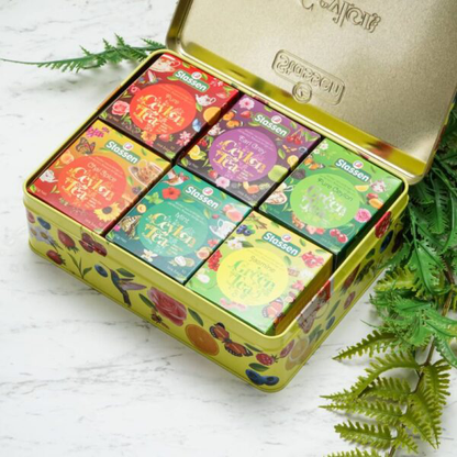 Kolorowe pudełka herbat Stassen obok filiżanki naparu i kwiatów.