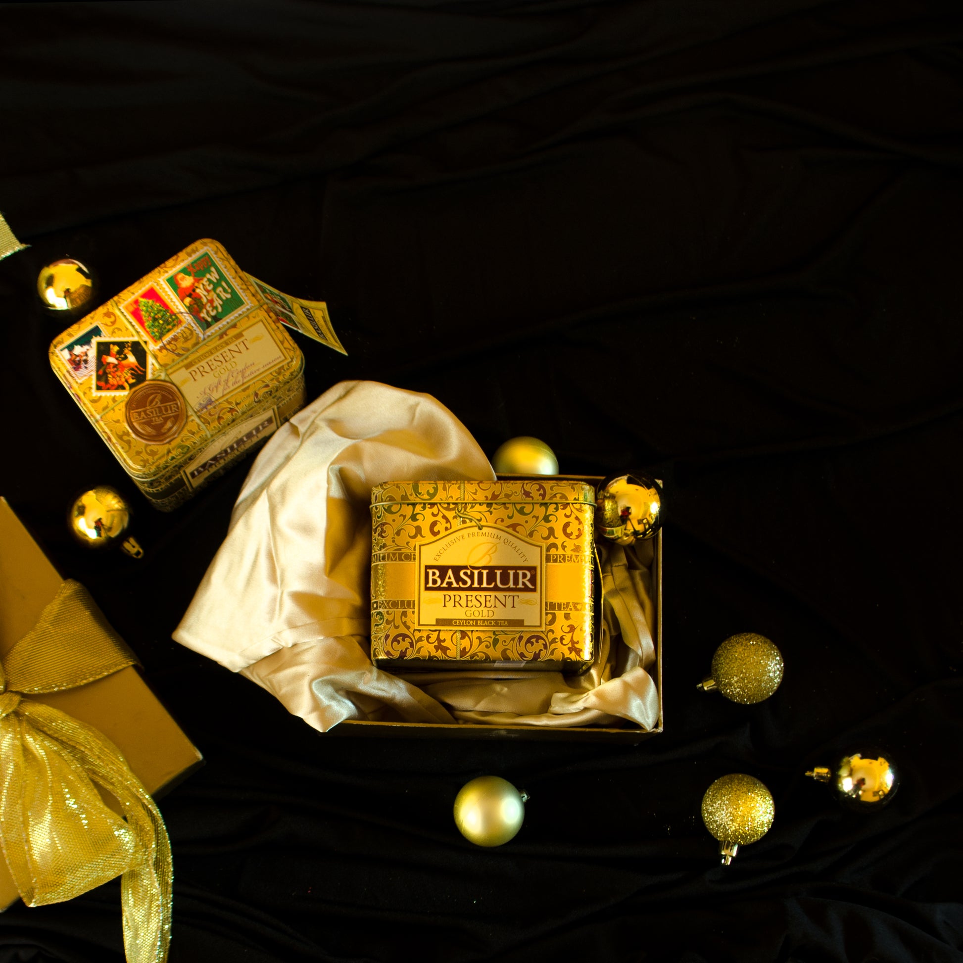 Złota puszka herbaty Basilur Present Gold ułożona w ozdobnym pudełku w otoczeniu świątecznych dekoracji.