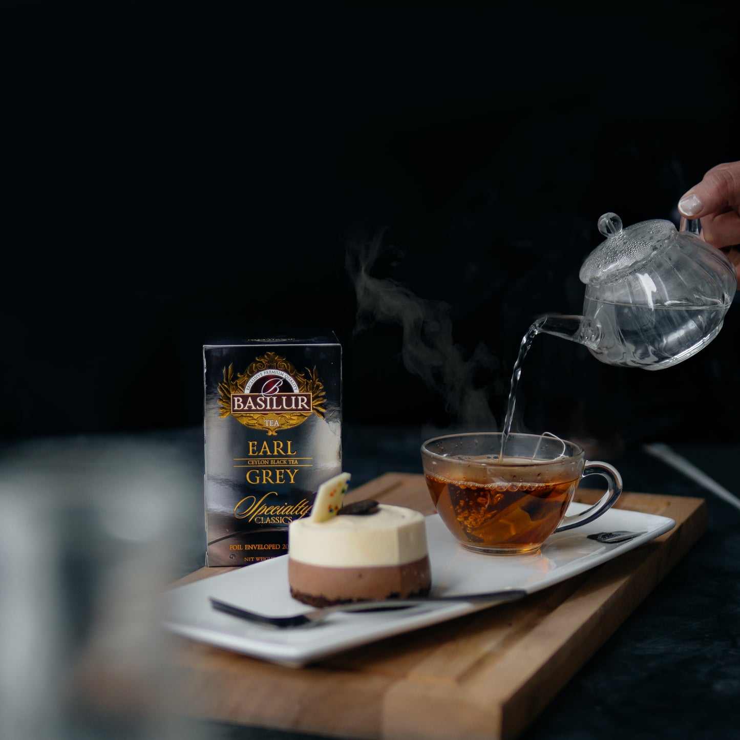 Opakowanie herbaty Basilur Earl Grey podane z deserem i szklanką, do której wlewany jest gorący napar.