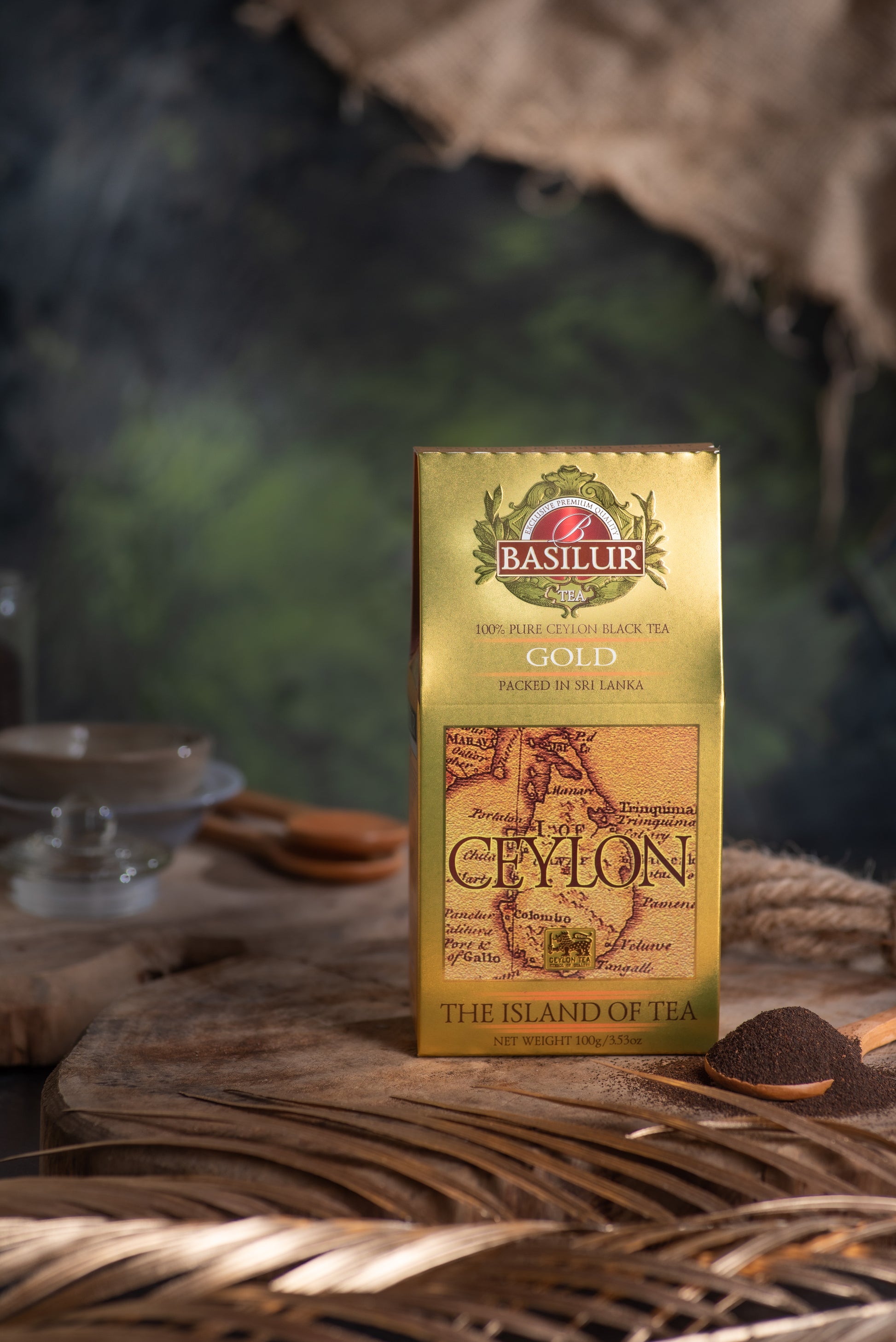 Złote opakowanie herbaty Basilur Gold ustawione na drewnianej podstawie obok łyżeczki z czarną herbatą.