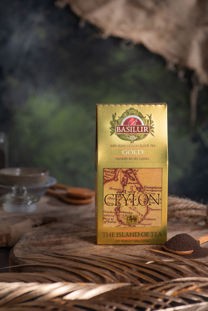 Złote opakowanie herbaty Basilur Gold ustawione na drewnianej podstawie obok łyżeczki z czarną herbatą.