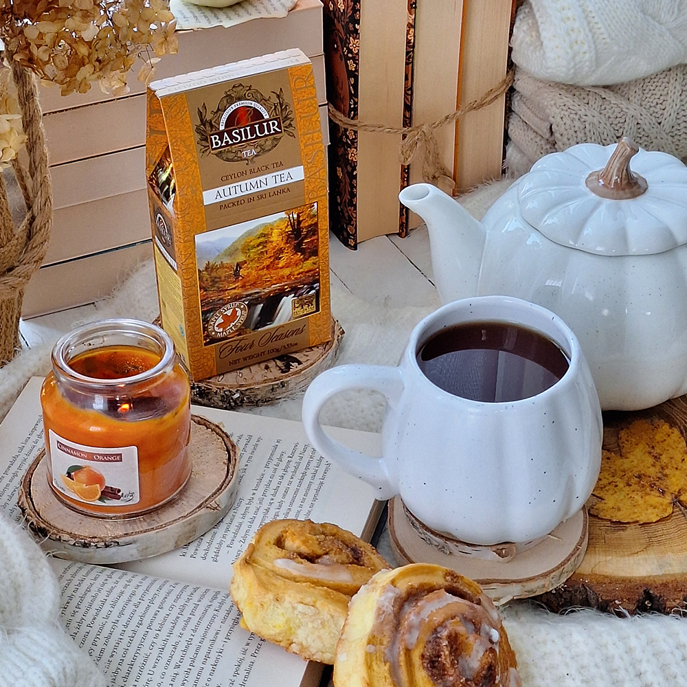 Basilur Autumn Tea przy filiżance czarnej herbaty, białym dzbanku, świecy i jesiennych dodatkach