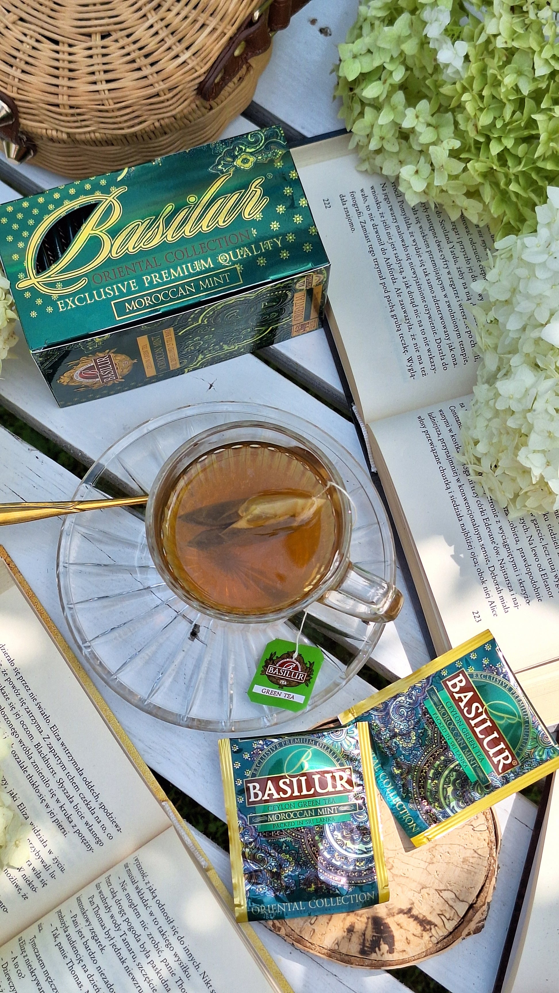 Herbata Basilur Moroccan Mint w kopertach zaprezentowana na stole obok filiżanki naparu.
