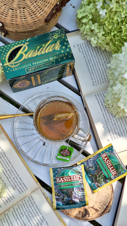 Herbata Basilur Moroccan Mint w kopertach zaprezentowana na stole obok filiżanki naparu.