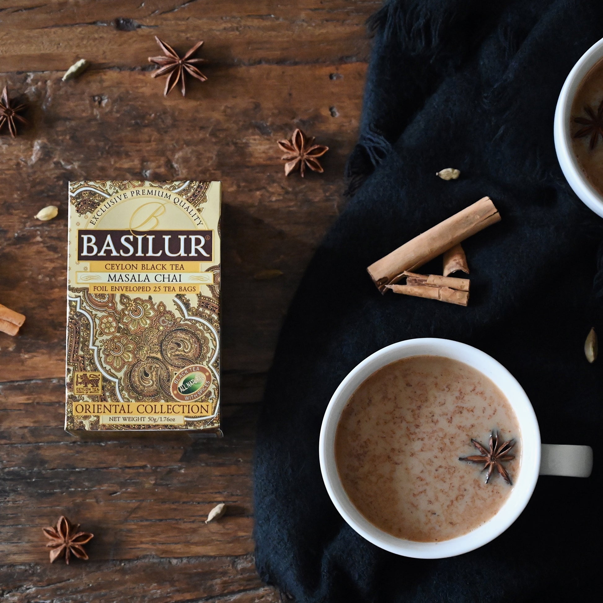 Herbata Basilur Masala Chai na drewnianym stole obok filiżanki chai latte, cynamonu i anyżu.