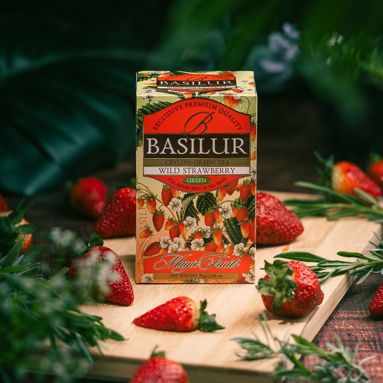 Zielona herbata Basilur Wild Strawberry w pudełku otoczonym świeżymi truskawkami.