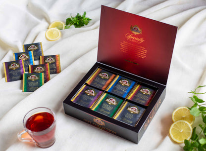 Otwarte pudełko Basilur Gift Collection Specialty Classics prezentujące kolorowe saszetki herbat takich jak Darjeeling Sencha Green Ceylon Premium English Afternoon English Breakfast oraz Earl Grey. Wokół znajdują się plasterki cytryny swieża mięta oraz filiżanka zaparzonej herbaty co podkreśla elegancki charakter klasycznej kolekcji.