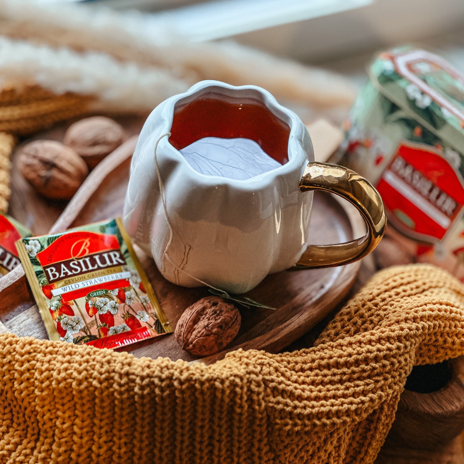 Herbata Basilur Wild Strawberry z filiżanką naparu, saszetkami i ciepłą domową aranżacją