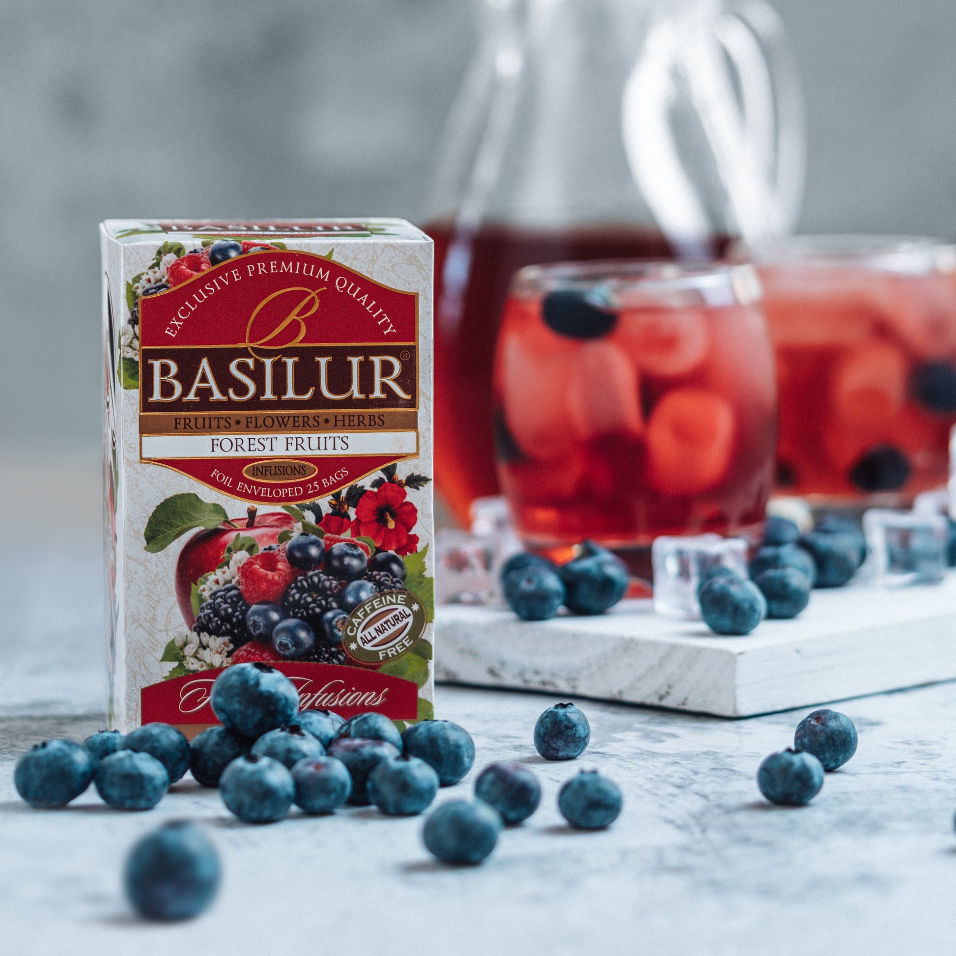 Opakowanie herbaty Basilur Forest Fruits otoczone borówkami obok dzbanka i szklanek z owocowym naparem.