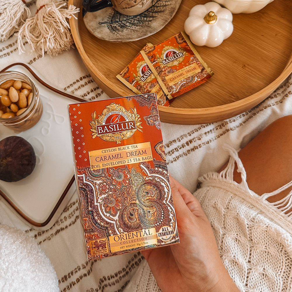 Opakowanie herbaty Basilur Caramel Dream z saszetkami, orzechami i jesiennymi dekoracjami na drewnianej tacy.