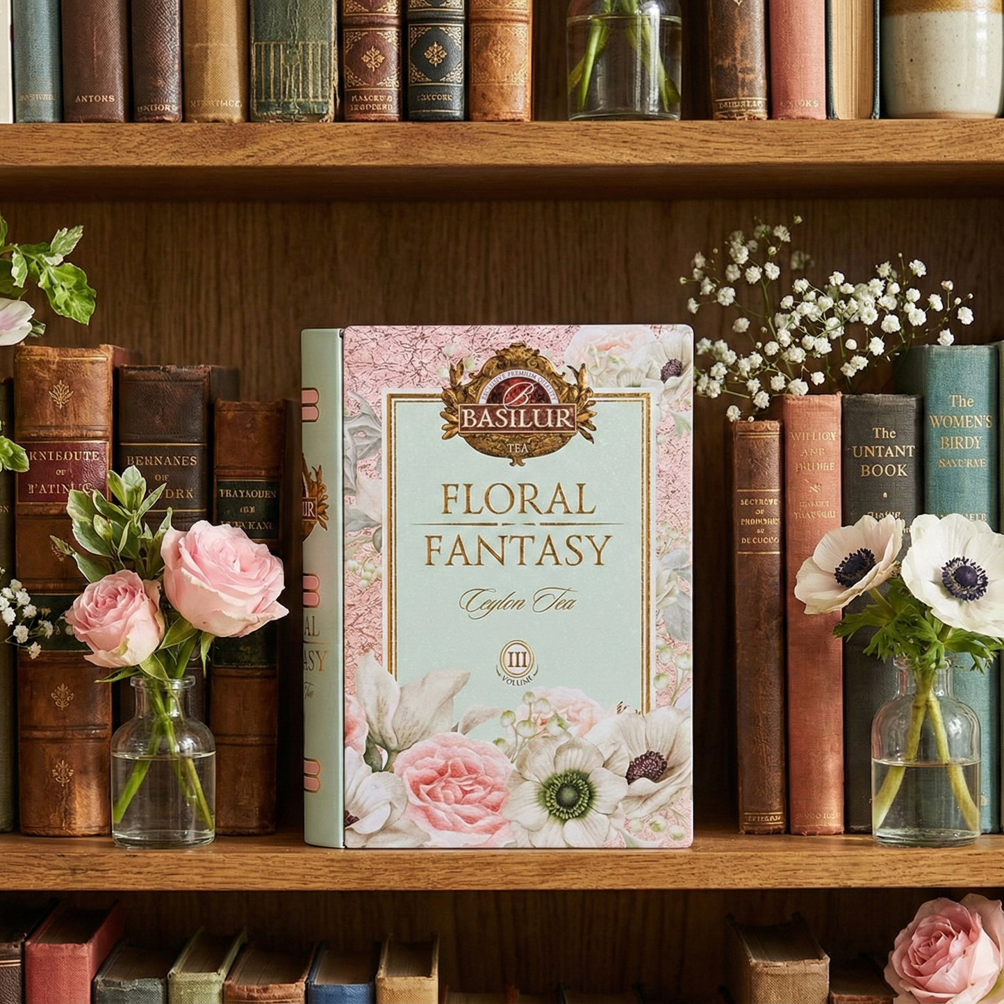 Elegancka herbata Basilur Floral Fantasy w puszce w formie książki, ustawiona na drewnianej półce wśród książek i kwiatów.