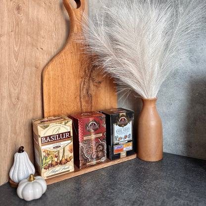 Opakowania herbat Basilur Ginger, Caramel Dream i Earl Grey Assorted ustawione przy drewnianych deskach i ozdobnym wazonie.