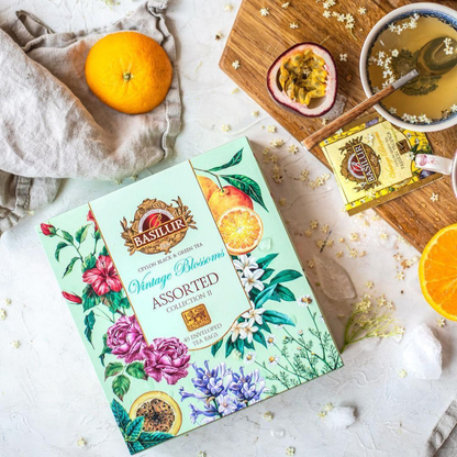 Zestaw herbat Basilur Vintage Blossoms Collection II na stole z filiżanką herbaty i owocami.