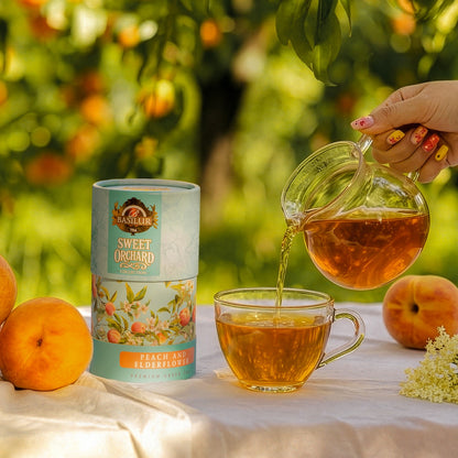 Herbata Basilur Peach and Elderflower obok filiżanki z naparem, dzbanka, brzoskwiń i kwiatów czarnego bzu