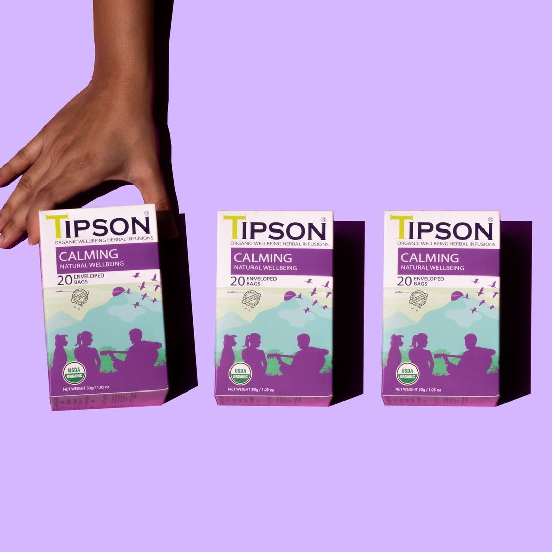 Trzy opakowania herbaty Tipson Calming Natural Wellbeing ustawione obok siebie na fioletowym tle.