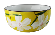 Ceramiczna czarka do herbaty w żółtym kolorze, zdobiona białymi kwiatami i zielonymi liśćmi.