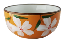 Ceramiczna czarka do herbaty w pomarańczowym kolorze, zdobiona białymi kwiatami i zielonymi liśćmi.