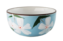 Ceramiczna czarka do herbaty w błękitnym kolorze, zdobiona białymi kwiatami i zielonymi liśćmi.