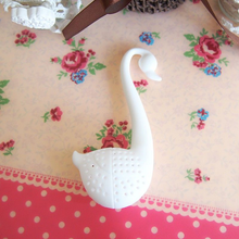 Zaparzacz silikonowy Biały Łabędź leżący na stole w otoczeniu kwiatowych motywów.