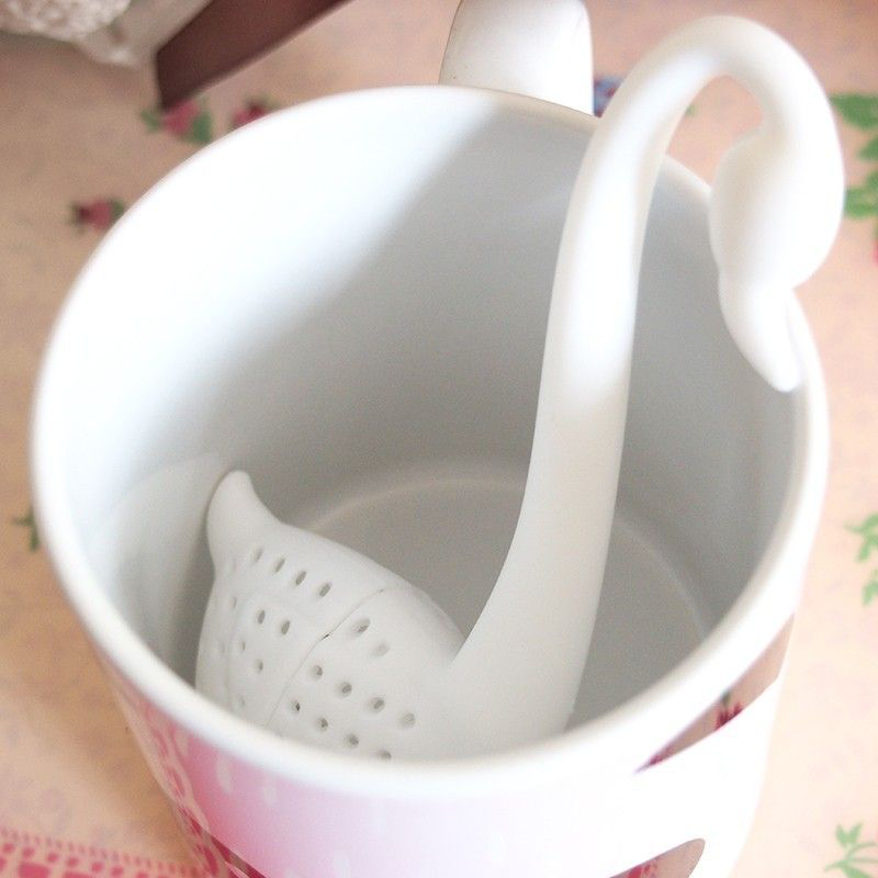 Silikonowy zaparzacz do herbaty w kształcie białego łabędzia umieszczony w kubku.