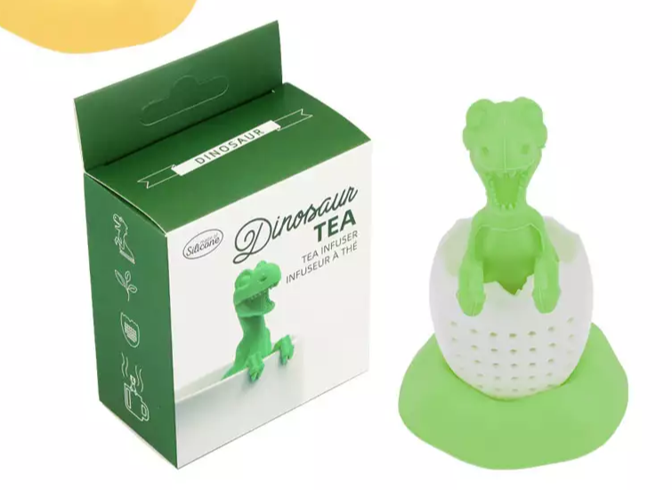 Zaparzacz silikonowy przedstawiający dinozaura wyłaniającego się z białego jajka obok pudełka.