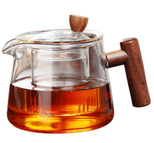 Szklany czajnik z zaparzaczem i drewnianym uchwytem wypełniony herbatą.