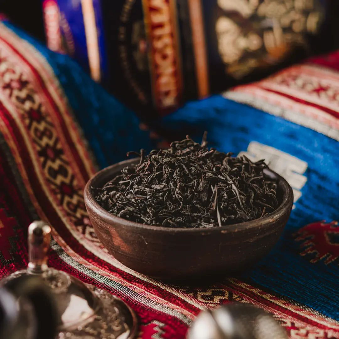 Suszone liście czarnej herbaty Kingsleaf Large Leaf OPA w brązowej miseczce na kolorowej tkaninie.