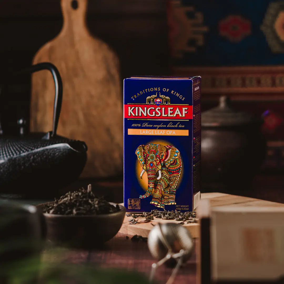 Opakowanie herbaty Kingsleaf Large Leaf OPA ustawione na drewnianym blacie w eleganckiej aranżacji.