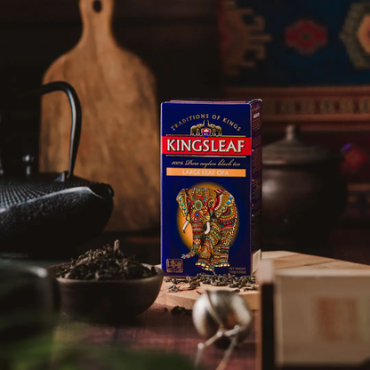 Opakowanie herbaty Kingsleaf Large Leaf OPA ustawione na drewnianym blacie w eleganckiej aranżacji.