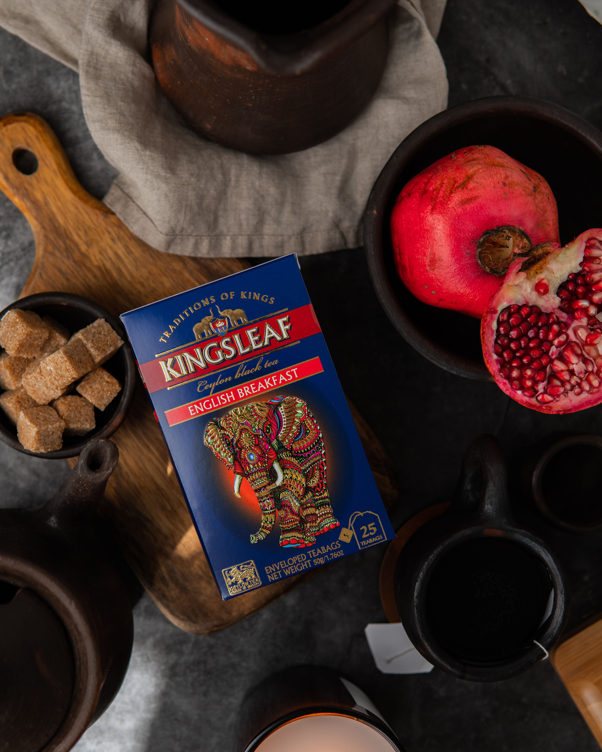 Pudełko herbaty Kingsleaf English Breakfast w otoczeniu granatów, cukru trzcinowego i ceramiki.