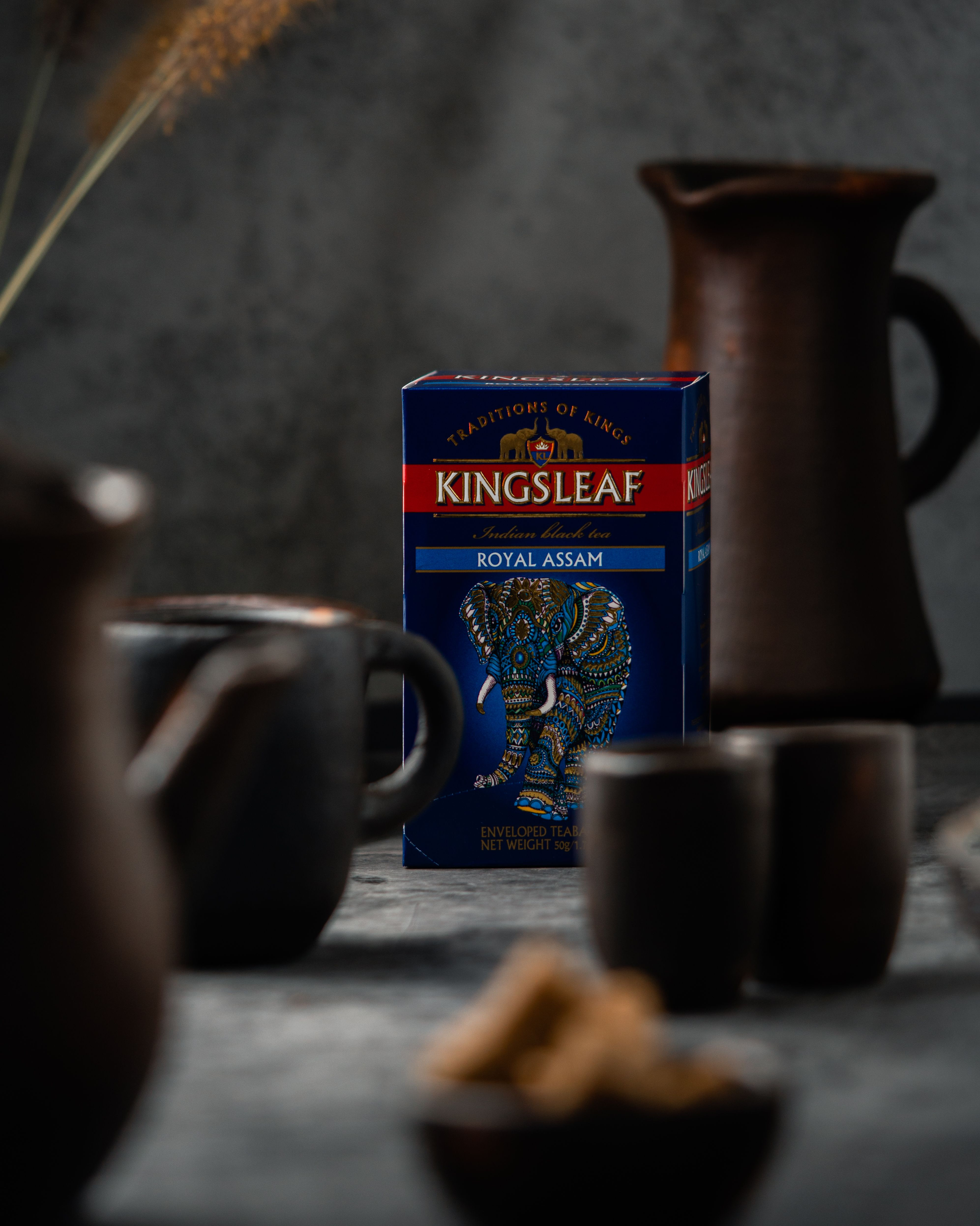Stylizowane zdjęcie Kingsleaf Royal Assam na stole w otoczeniu filiżanek i dzbanków.