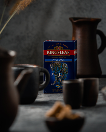 Stylizowane zdjęcie Kingsleaf Royal Assam na stole w otoczeniu filiżanek i dzbanków.
