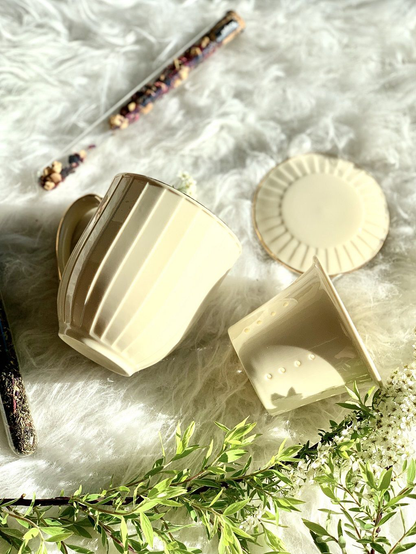 Kubek porcelanowy Nina 400 ml w odcieniu ecru z zaparzaczem i pokrywką obok, na tle dekoracyjnych elementów.