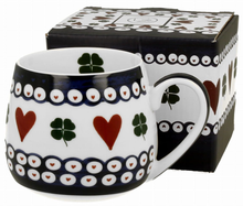 Zestaw: kubek baryłka Indigo 3 z dekoracją w serca i koniczyny, ustawiony obok dopasowanego opakowania.