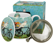 Kubek porcelanowy baryłka z zaparzaczem i pokrywką w zestawie, wzór biały kot na rowerze, w tle pudełko ozdobne.