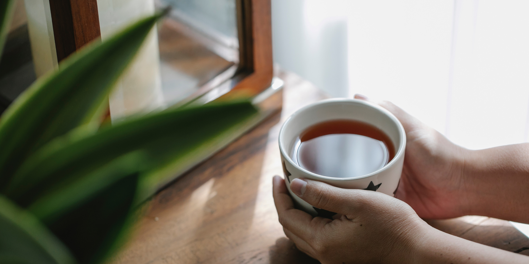 Porcelanowy kubek z czarną herbatą otulony dłońmi. 