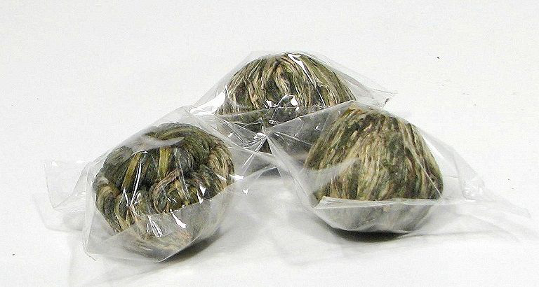 Zbliżenie na trzy kulki herbaty rozkwitającej Flower Pearl zapakowane w folię.