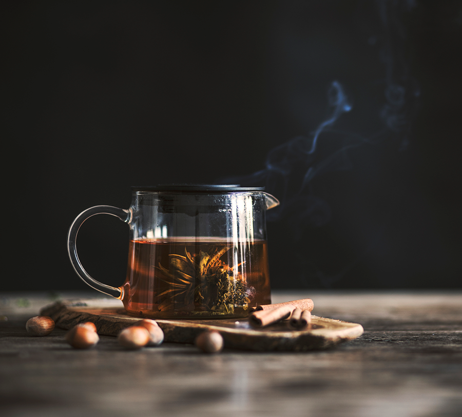 Herbata rozkwitająca Golden Yuanbao w szklanym dzbanku na drewnianym tle, parujący napar z nutą ciepła i elegancji.