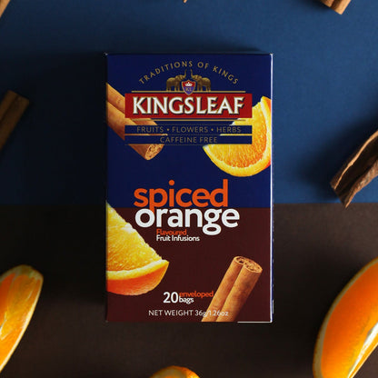 Opakowanie herbaty Kingsleaf Spiced Orange na tle pomarańczy i lasek cynamonu, aromatyczna owocowa infuzja bez kofeiny.