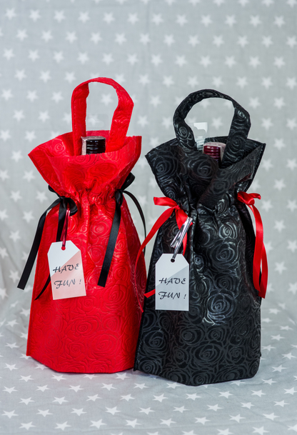 Dwa worki prezentowe – czerwony i czarny z tłoczonym wzorem róż, rączkami i ozdobnymi wstążkami, w środku butelki wina.