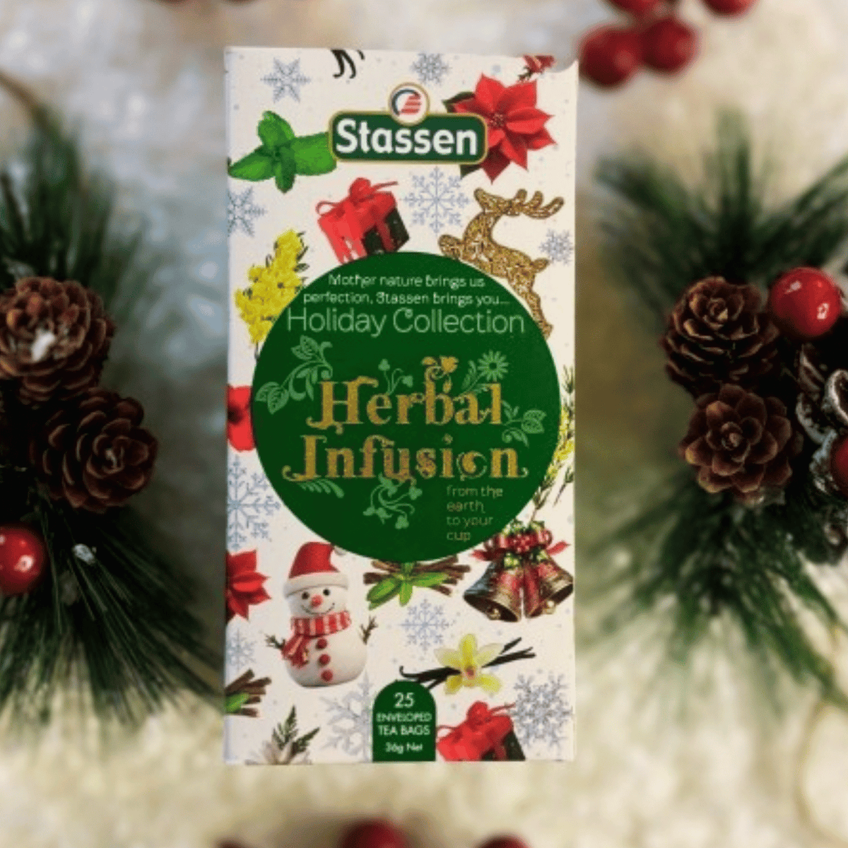 Zestaw herbat Stassen Holiday Collection 25 kopert w świątecznym pudełku z bałwankiem i reniferem, w otoczeniu gałązek świerku i szyszek.