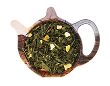 Zielona herbata Sencha Imbir i Pigwa z kawałkami imbiru, skórką pomarańczową i morelą suszoną przedstawiona na podstawce w kształcie czajniczka